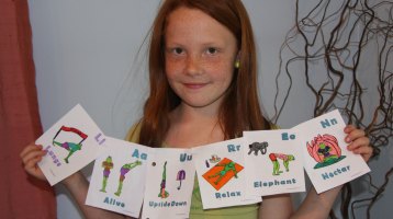 a girl holds up a banner she made with the best kids yoga teacher training printable Yoga alphabet