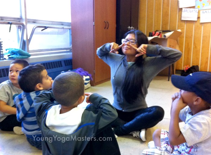 a kids yoga teacher points to her nose as she takes a deep breath in and 4 kids follow along doing yoga breathing