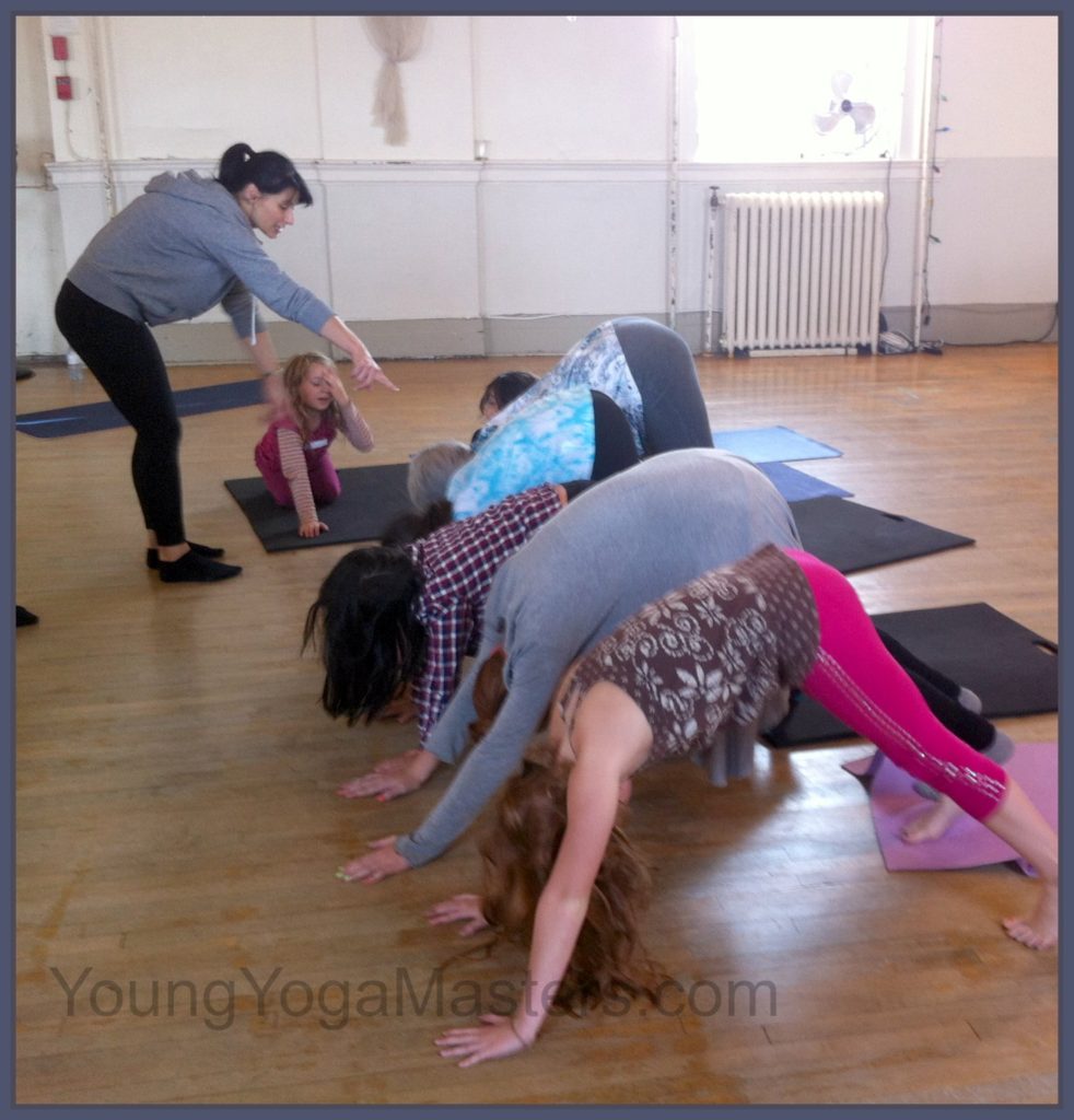A teacher points to the row of children doing downward dog forming a tunnel after a child has bumped her head. 