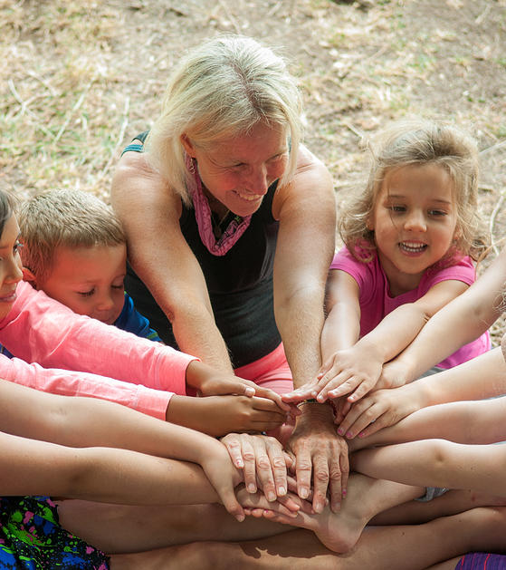 Macy Ratliff teaches a group yoga pose to children with the sitting forward bend making a big flower