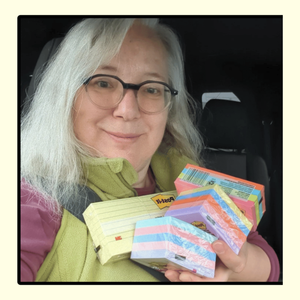 Aruna sits in her car, she holds a big handful of colourful post it notes and smiles.