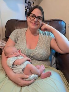 A new mother sits in a comfy chair holding a newborn cradled in her arm.