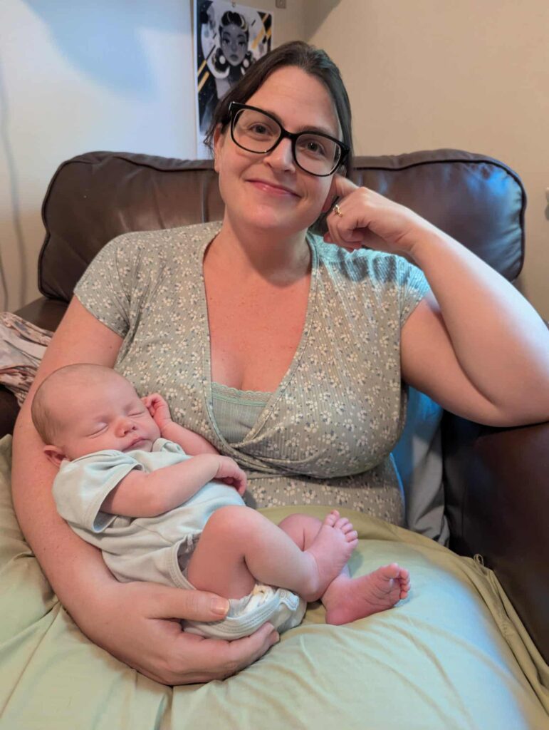 A new mother sits in a comfy chair holding a newborn cradled in her arm.